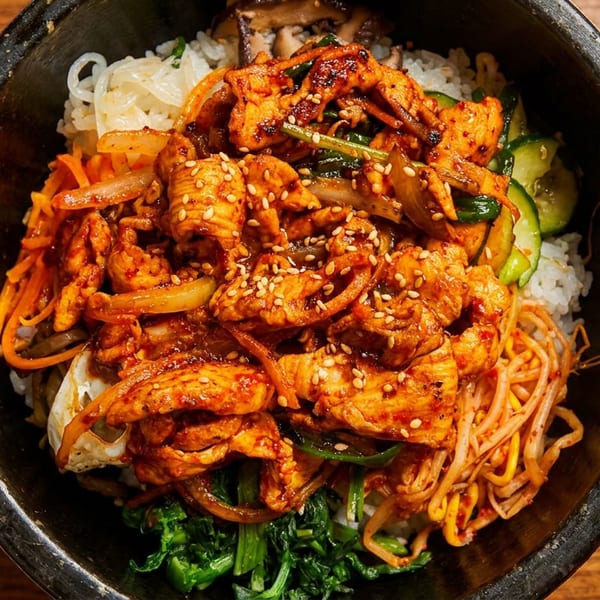 Spicy chicken bibimbap with rice and colorful vegetables in a dark stone bowl.