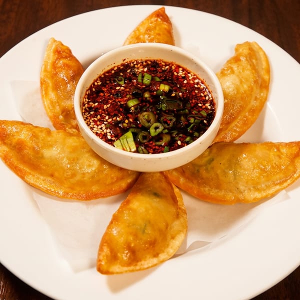 Golden fried dumplings on a white plate with a central bowl of chili-sesame dipping sauce.