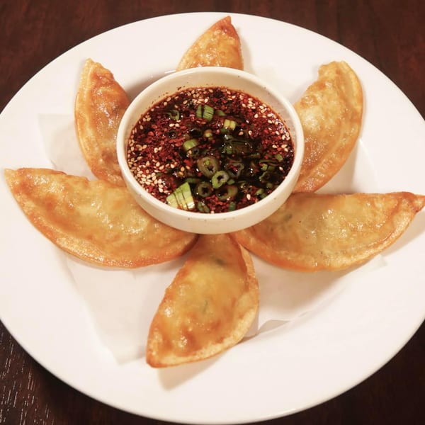 A plate of golden fried dumplings surrounding a bowl of chili-sesame dipping sauce.