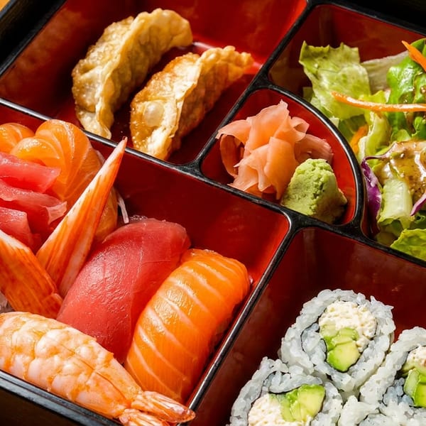 A bento box filled with sushi, sashimi, gyoza, salad, and pickled ginger with wasabi.
