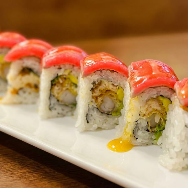 Eight sushi rolls with tempura shrimp, avocado, tuna, and yellow sauce on a white rectangular plate.