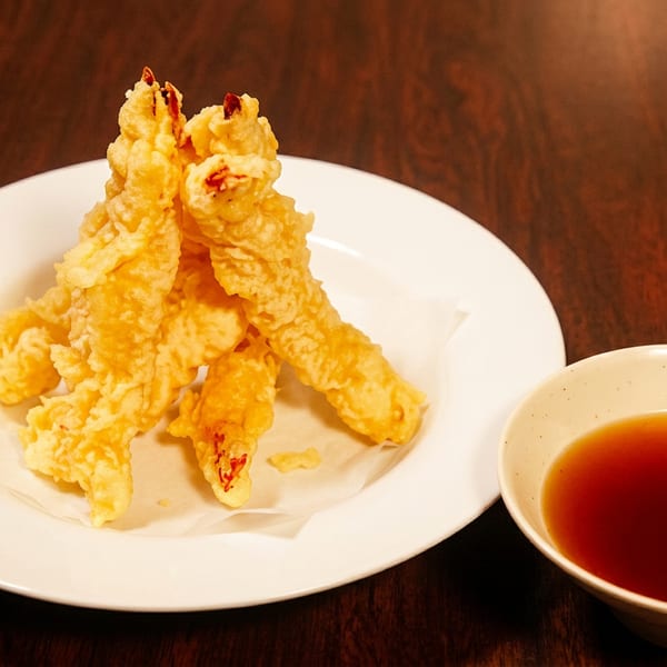 Golden fried tempura on a white plate with a small bowl of dipping sauce.