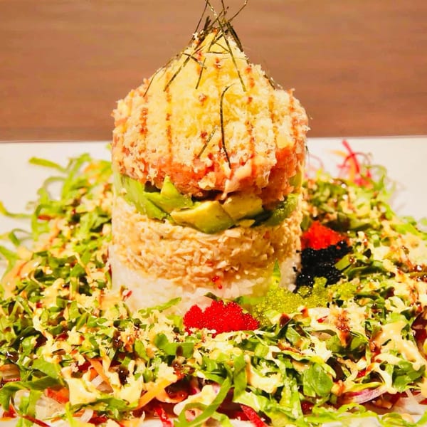 Vibrant layered sushi tower with rice, crab, avocado, spicy tuna, tempura, and colorful roe on a salad.
