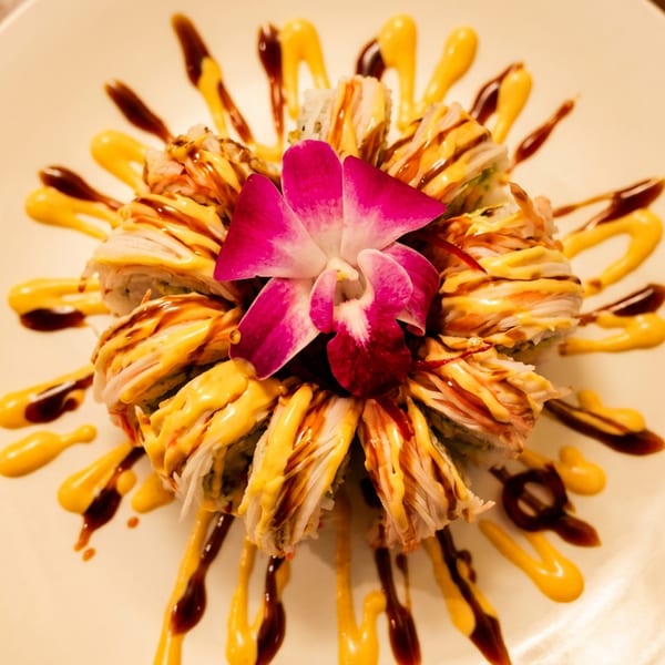 Artfully arranged sushi rolls with yellow and brown sauces, centered by a vibrant pink orchid.